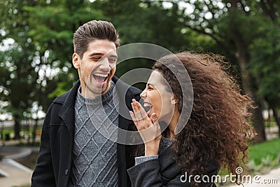 Image of satisfied couple man and woman 20s in warm clothes, walking through green park Stock Photo