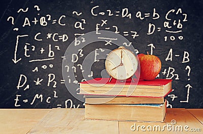 Image of school books on wooden desk, apple and vintage clock over black background with formulas. education concept Stock Photo