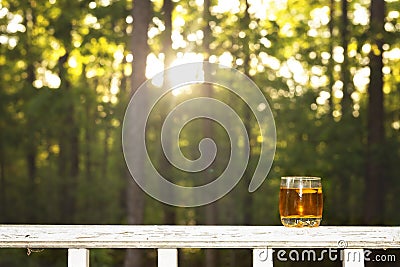 Image of a shot of whiskey on a porch railing in front of the sunset Stock Photo