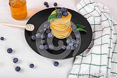 Image shows a homemade fluffy pancake with blueberry and mint on the top; situation is decorated with white wooden table and honey Stock Photo