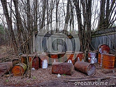 This image shows rusty barrels that are scattered in front of a wooden fence Stock Photo