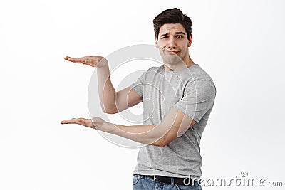 Image of skeptical brunette guy holding empty copy space between hands, showing hand box gesture as if display product Stock Photo
