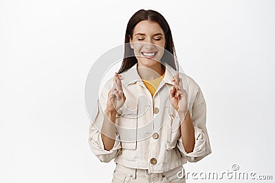 Image of smiling hopeful female model close eyes, fingers crossed and make wish, anticipating good news, relish positive Stock Photo