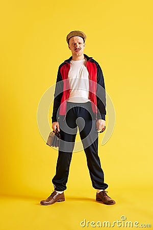 Image of squinting young sport coach dressed in sport wear and holding purse and cap over bright yellow studio Stock Photo