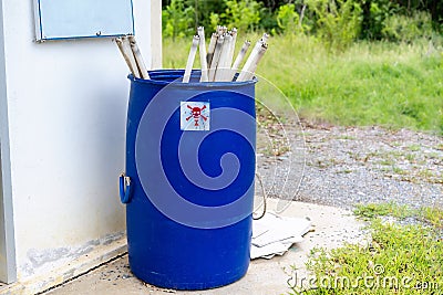 Image of a stack of disused and discarded neon lamp tubes waiting for recycling in the trash with skull mark in blue bin. Stock Photo