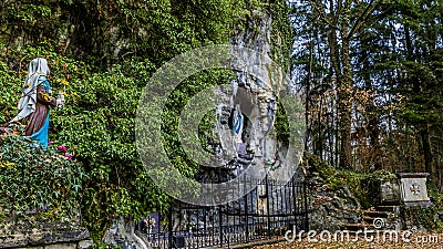 Image of a statue of Bernadette praying to Our Lady of Lourdes in a natural grotto Stock Photo