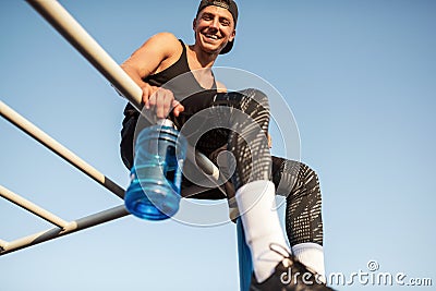 Image of stylish fitness male relaxing with blue bottle with water after workout outdoor. Sportsman in black sportswear hydrating Stock Photo