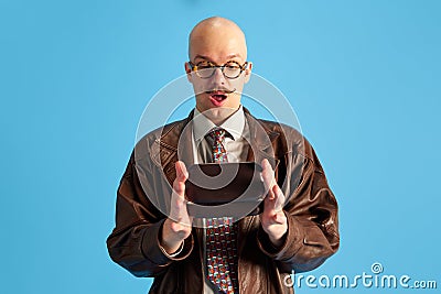 Image of surprised balded and mustache young man in glasses with box in hands over blue studio background. Stock Photo