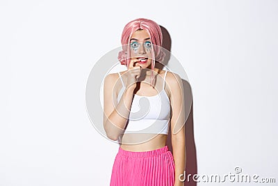 Image of timid cute girl in pink wig, looking indecisive and biting finger, standing over white background Stock Photo
