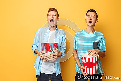 Image of two excited beautiful teenagers, guys watching an interesting movie and eating popcorn on a yellow background Stock Photo