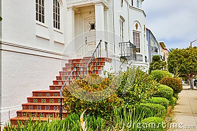 Unique staircase leading to white door on building with bushes and tunnel view down sidewalk Stock Photo