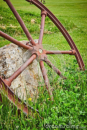 Vertical shot of rusty wheel resting against textured concrete block fragment in grassy field Stock Photo