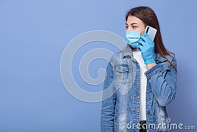 Image of woman afraids for getting Corona virus, talking to phone and looking aside, posing isolated over blue studio background, Stock Photo