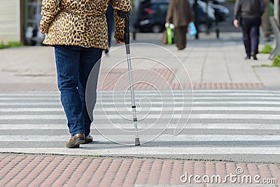 Woman with a crutch at a pedestrian crossing, rear view Stock Photo