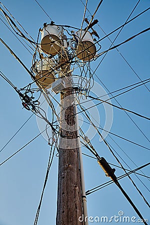 Wooden telephone pole with three barrels on top and lots of converging phone lines on a clear blue sky Stock Photo