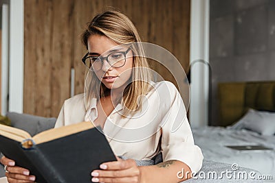 Image of young concentrated woman reading book while sitting on couch Stock Photo