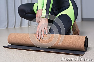 Image of a young woman in a gymnastics suit rolling up a mat after a workout. The concept of fitness, yoga, pilates Stock Photo
