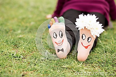 Images of lovely groom and bride just married painted in bright colors on feet of child outdoor at summer. Stock Photo