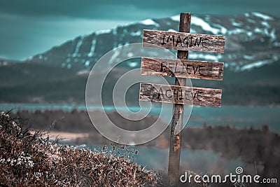imagine believe achieve text quote engraved on wooden signpost outdoors in landscape looking polluted Stock Photo