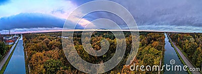 Autumn Tapestry: Aerial View of River or Canal Flowing Through Colorful Woods Under a Dramatic Cloudy Sky Stock Photo