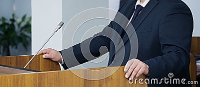 An important man - a lawyer, businessman, politician, or official speaks to the public, leaning his hands on the podium. Official Stock Photo