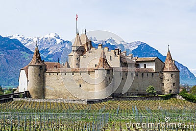 Imposing medieval Aigle castle atop a small hill, surrounded by majestic snow-capped mountain peaks Stock Photo