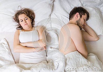 Impotence concept. Young man is sleeping in bed. Sad, disappointed and unsatisfied girlfriend. Stock Photo