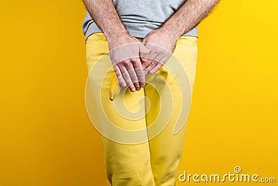 Impotence and men`s health. A man in yellow jeans shyly covers a banana near the genitals with his hands. Yellow background. Clos Stock Photo