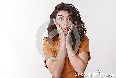 Impressed surprised excited attractive curly-haired young woman widen eyes press palms cheeks unbelievable luck say wow Stock Photo