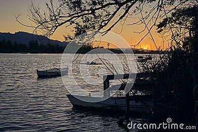 Impressive sunset on the lake from the jetty with some boats floating and a tree in the foreground framing the picture Stock Photo