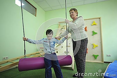 Improving motor control: female therapist helping Down syndrome boy to do exercises at the rehabilitation room Editorial Stock Photo