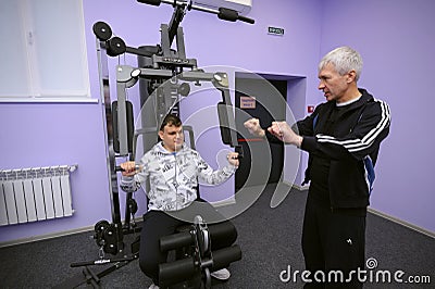 Improving motor control. Man therapist teaching disabled boy of training on the exersice machine. Municipal Department Editorial Stock Photo