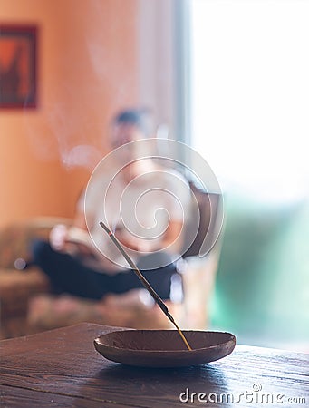 Incense stick burning with a woman sitting crosslegged in the background in a cozy room Stock Photo