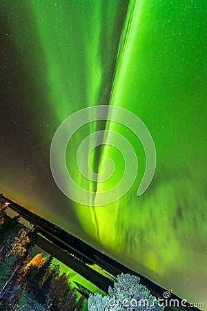 Inclined earth and bright green aurora lights almost on the whole sky over tree tops in Sweden, river, city lights and lake, clear Stock Photo
