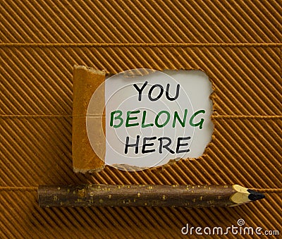 Inclusion and belonging symbol. Words `You belong here` appearing behind torn brown paper. Beautiful brown background. Business, Stock Photo