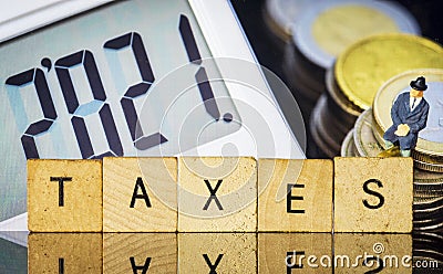 Income Tax Campaign 2021. Taxman sitting on coin stack. TAXES sign Macro Stock Photo