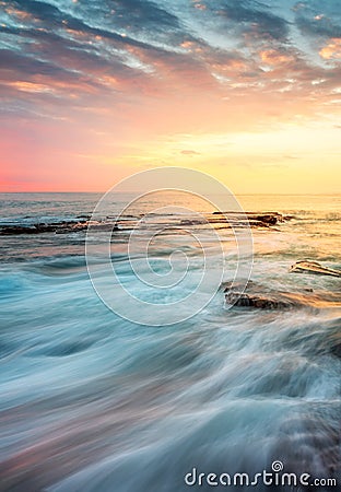 Incoming waves wash over rocks at sunrise Stock Photo
