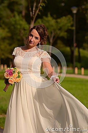 Incredibly beautiful bride with bouquet of roses. Romantic accessory of fiancee. Long haired girl in wedding gown Stock Photo