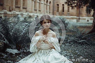 An incredibly beautiful princess sits in the castle garden amid the fern and moss. A beautiful, frightened face. Big sad Stock Photo