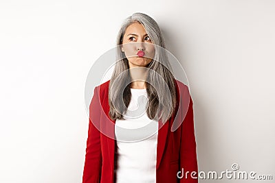 Indecisive asian businesswoman pucker lips and looking thoughtful at upper left corner, standing over white background Stock Photo