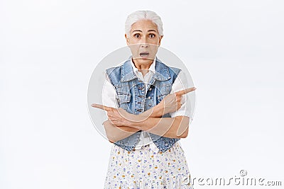 Indecisive worried old woman with grey hair, look hesitant and unsure pointing sideways, left and right with crossed Stock Photo
