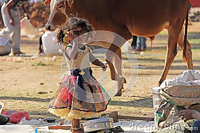 India, Hampi, 02 February 2018. A small poor and dirty Indian girl playing with sunglasses. A little girl in big glasses from the Editorial Stock Photo