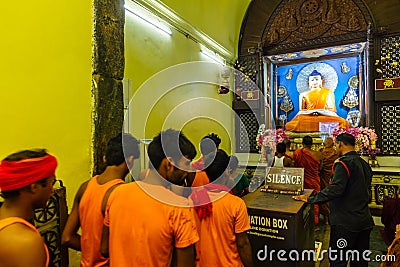 Indian Buddhist monk and people standing and praying on bare foot in front of large statue of lord Buddha inside Mahabodhi Temple. Editorial Stock Photo