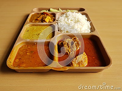 Indian chicken thali with rice dal chicken salad vegetable curry on a plastic segmented plate in wooden background Stock Photo