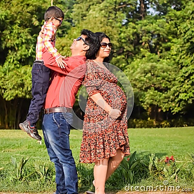 Indian couple posing for maternity baby shoot with their 5 year old kid. The couple is posing in a lawn with green grass and the Stock Photo