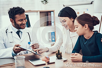 Indian doctor seeing patients in office. Doctor is showing clipboard to mother and daughter. Stock Photo