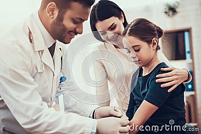 Indian doctor seeing patients in office. Doctor is putting patch on daughter`s arm. Stock Photo