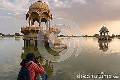 Indian female traveller, woman photographer taking picture of Chhatris and shrines with reflection of them on the water of Gadisar Editorial Stock Photo