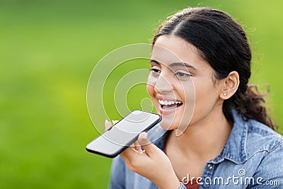 Indian lady dictating to phone on green field Stock Photo