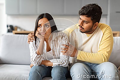 Indian man comforting his distressed girlfriend while sitting together on sofa Stock Photo